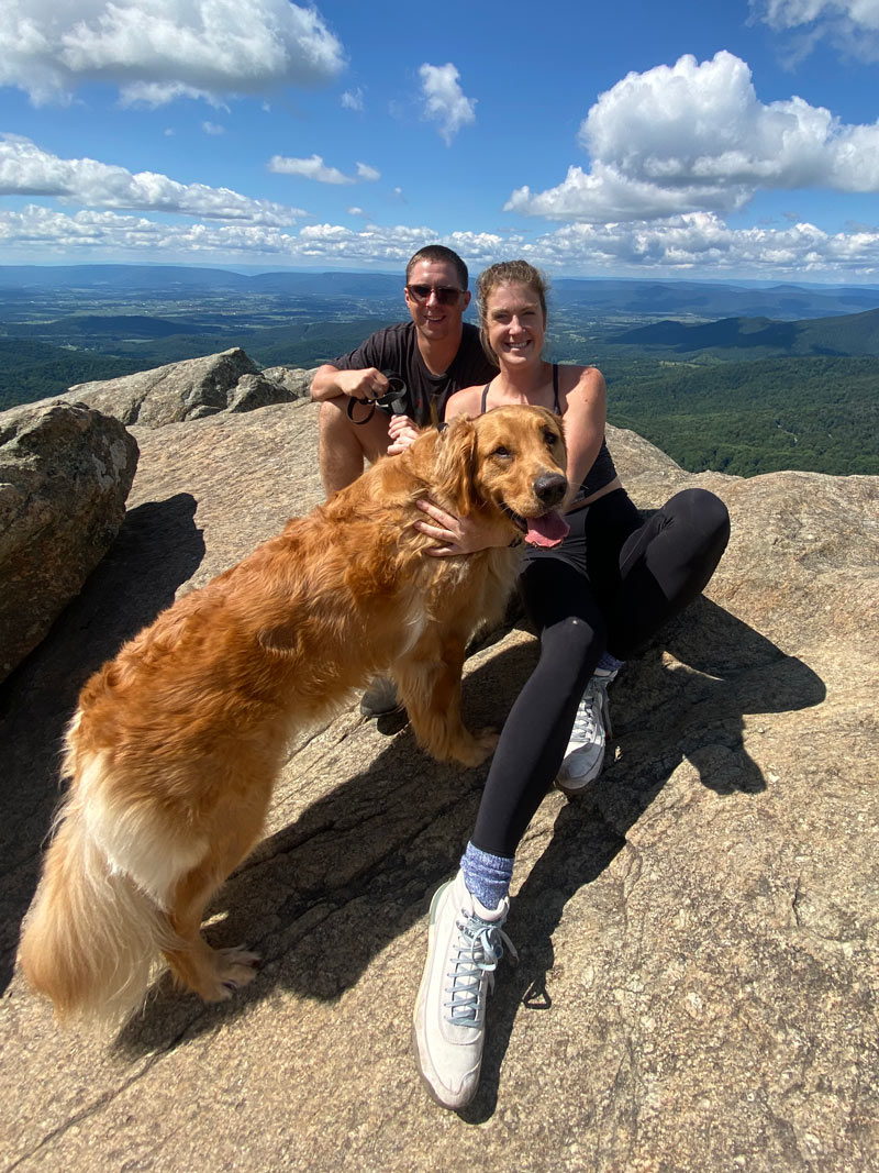 A photo of Sarah and her husband on a hike with their golden retriever.