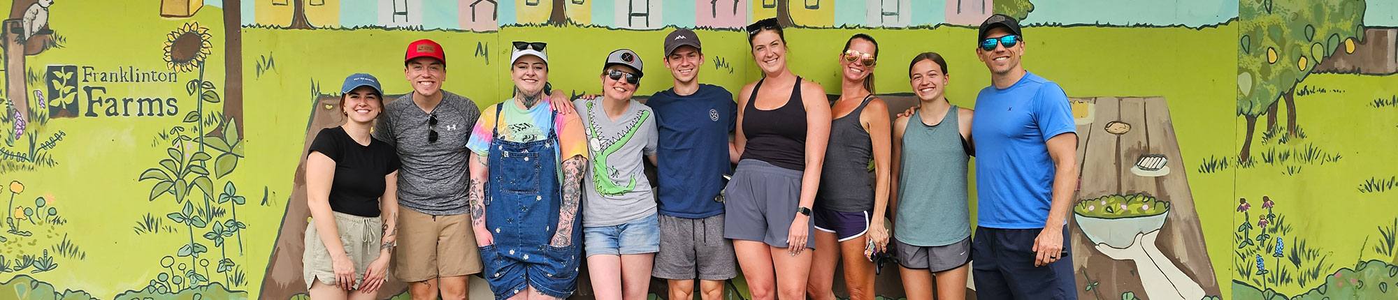 YLB team members stand in front of a mural after volunteering at Franklinton Farms
